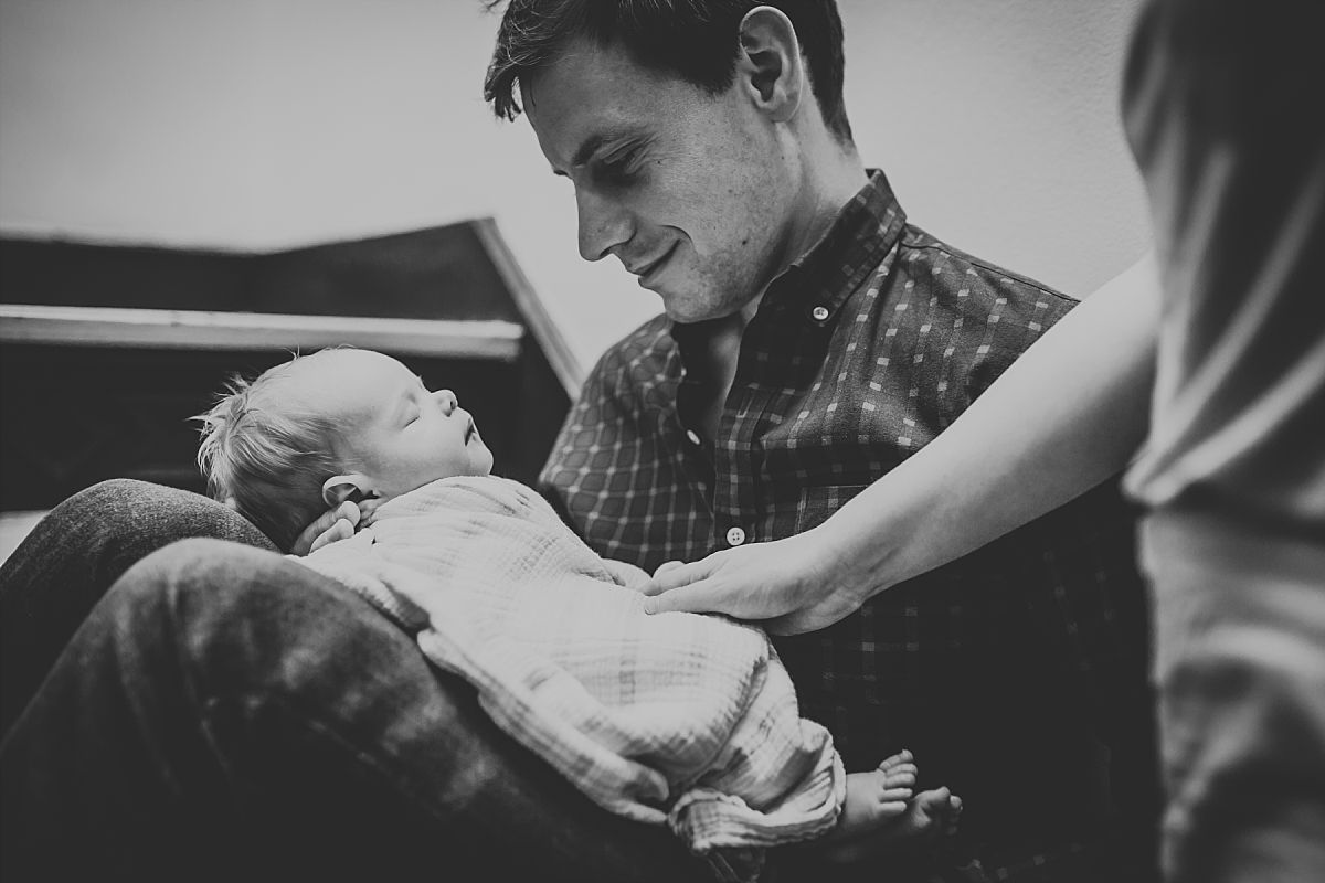 nyc family and newborn photographer mom, dad and newborn baby girl sit in stairwell while newborn sleeps on dad's lap