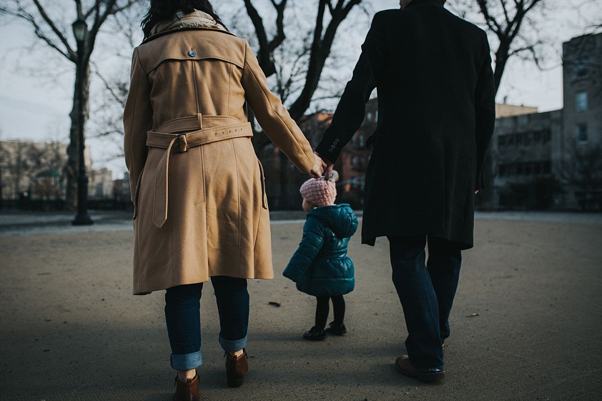 nyc family and newborn photographer mom and dad hold hands and toddler daughter walks in front in nyc park