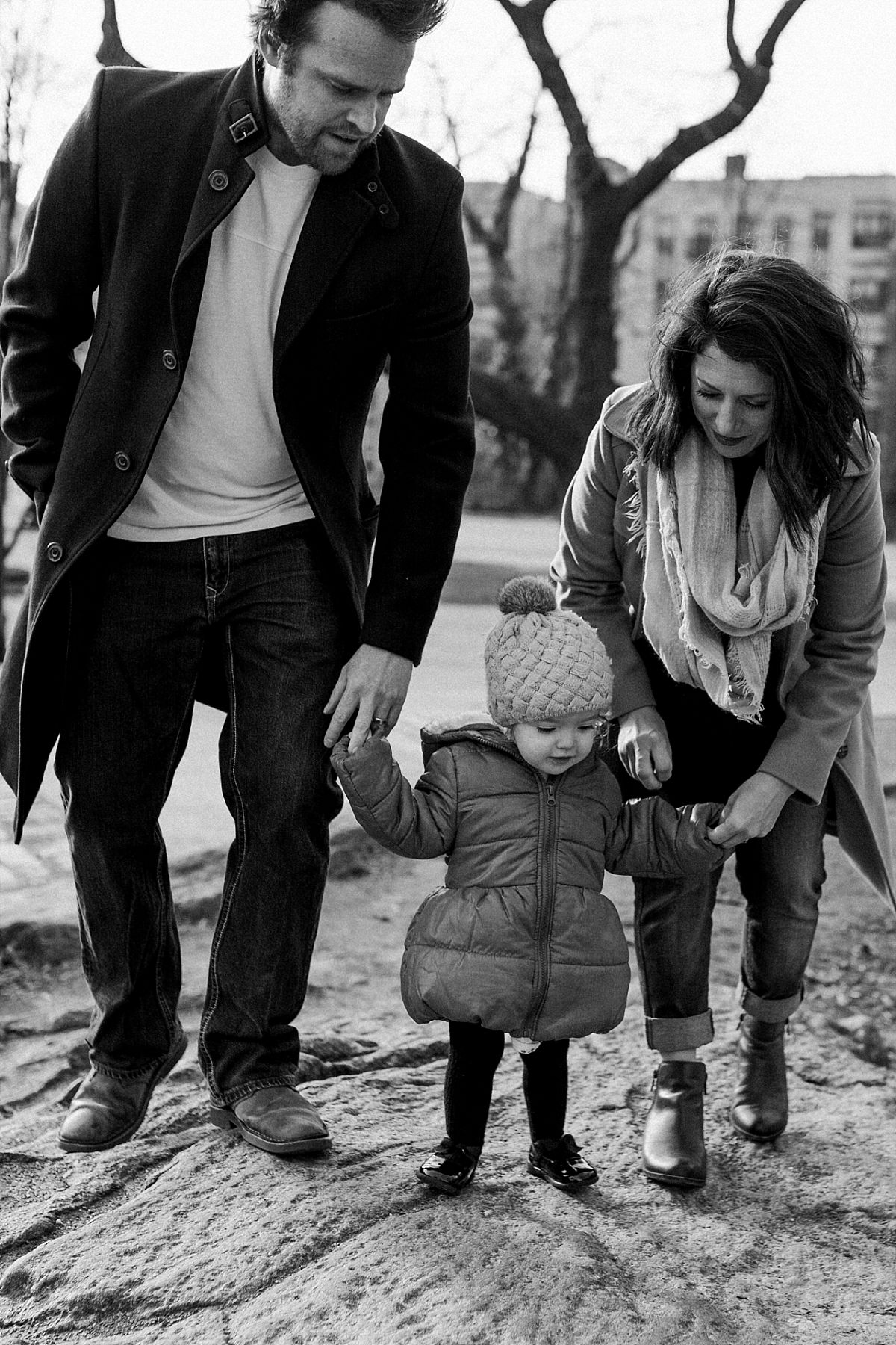 nyc family and newborn photographer mom, dad and daughter hold hands climbing rock in nyc park