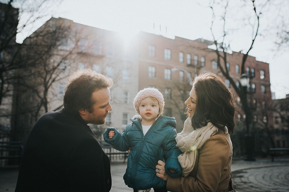 nyc family and newborn photographer, mom, dad and toddler enjoy the sun sitting on nyc park bench