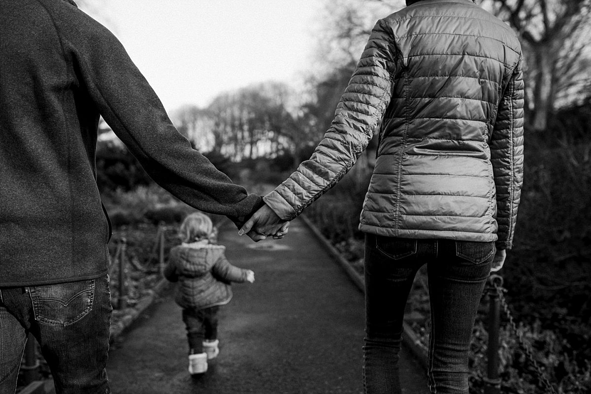 nyc family and newborn photographer mom and dad hols hands and toddler skips in front in nyc park