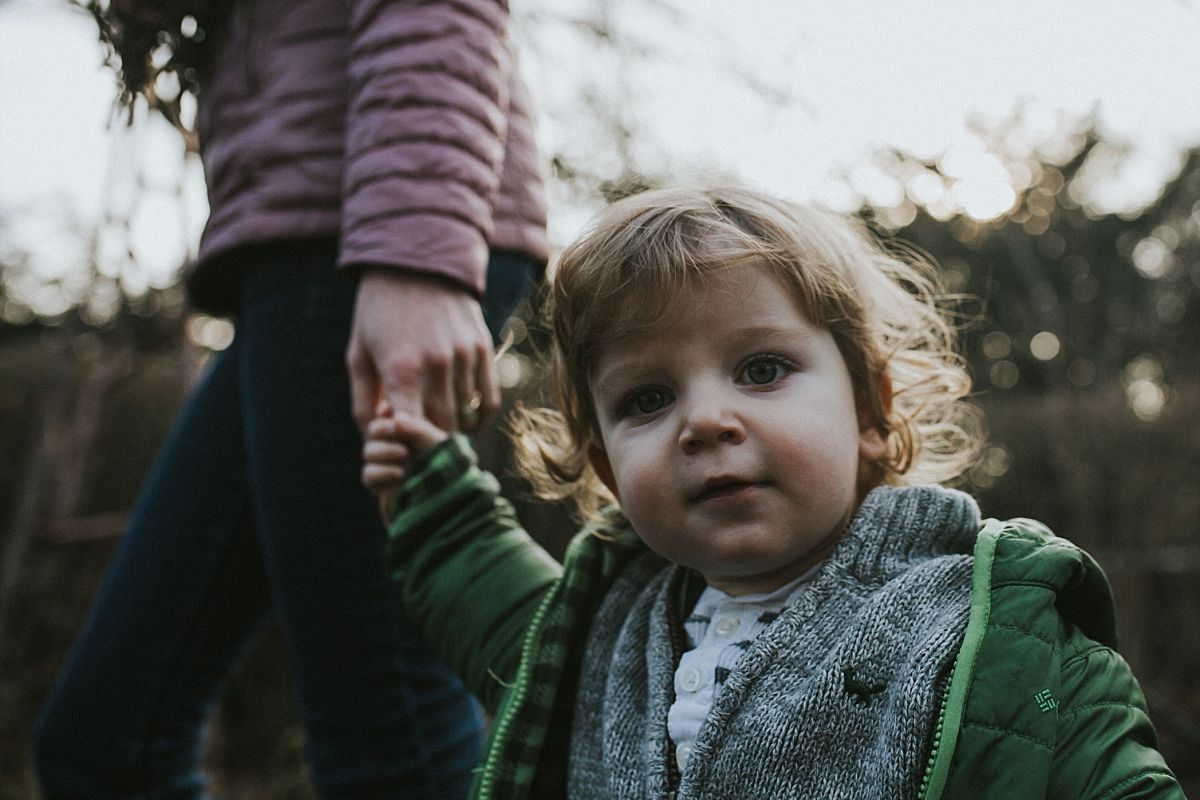 nyc family and newborn photographer mom holds toddlers hand walking on nyc park path in fun outdoor family session