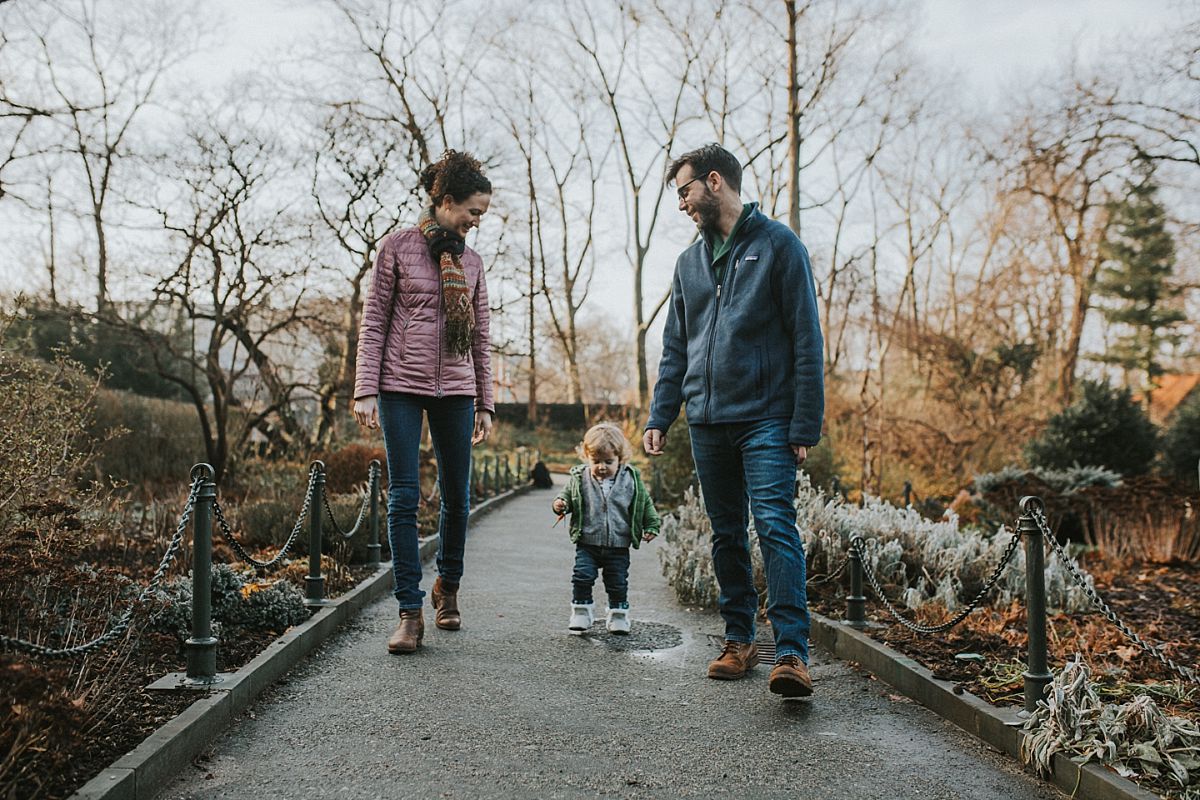nyc family and newborn photographer mom, dad and toddler walk on footpath in lifestyle family session outside in nyc park