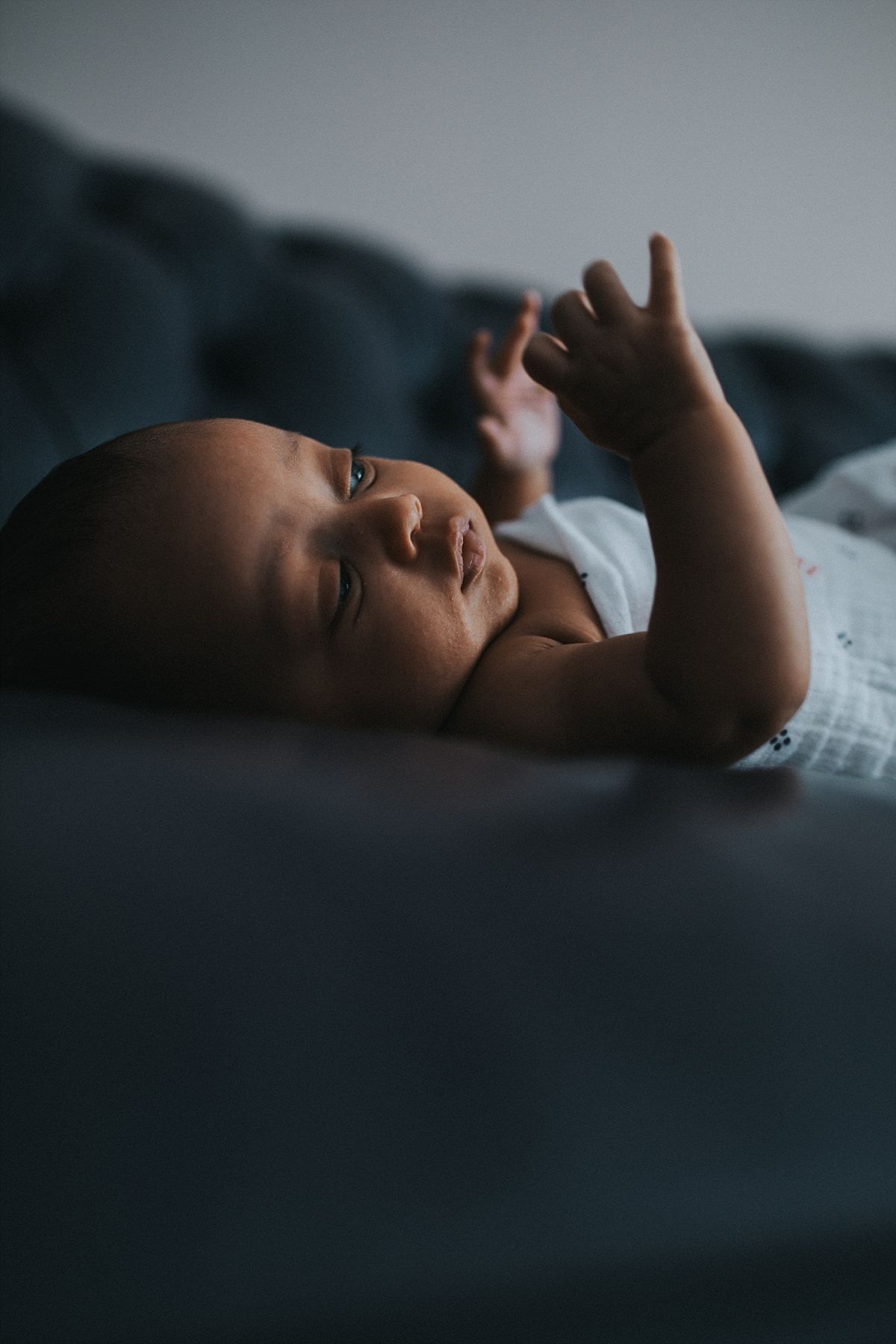 nyc family and newborn photographer newborn girl lies on couch and stetches arms out in mommy and me session