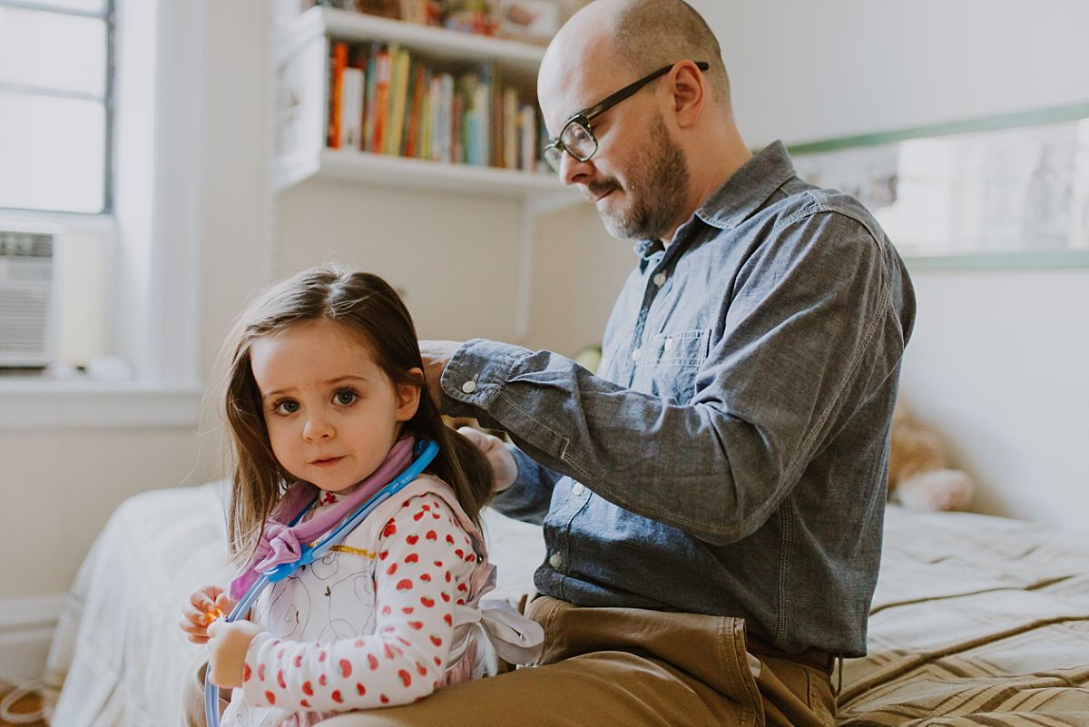 nyc family and newborn photographer dad brushes toddler's hair while sitting on bed