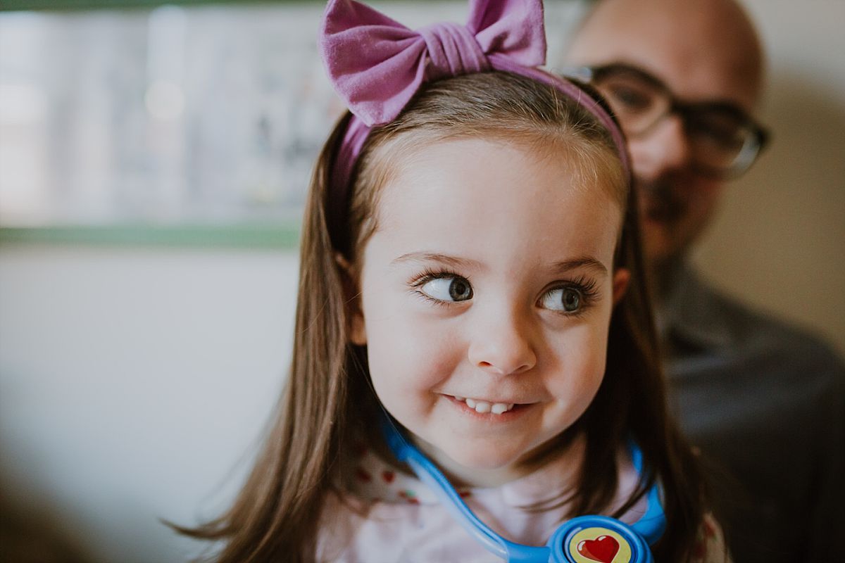 nyc family and newborn photographer daughter sits on bed with purple bow in hair
