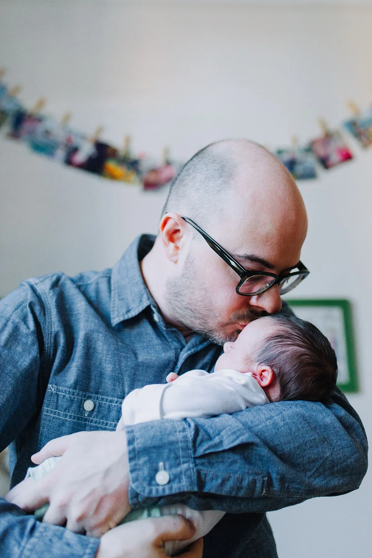 nyc family and newborn photographer dad holds newborn girl and kisses her gently on forehead