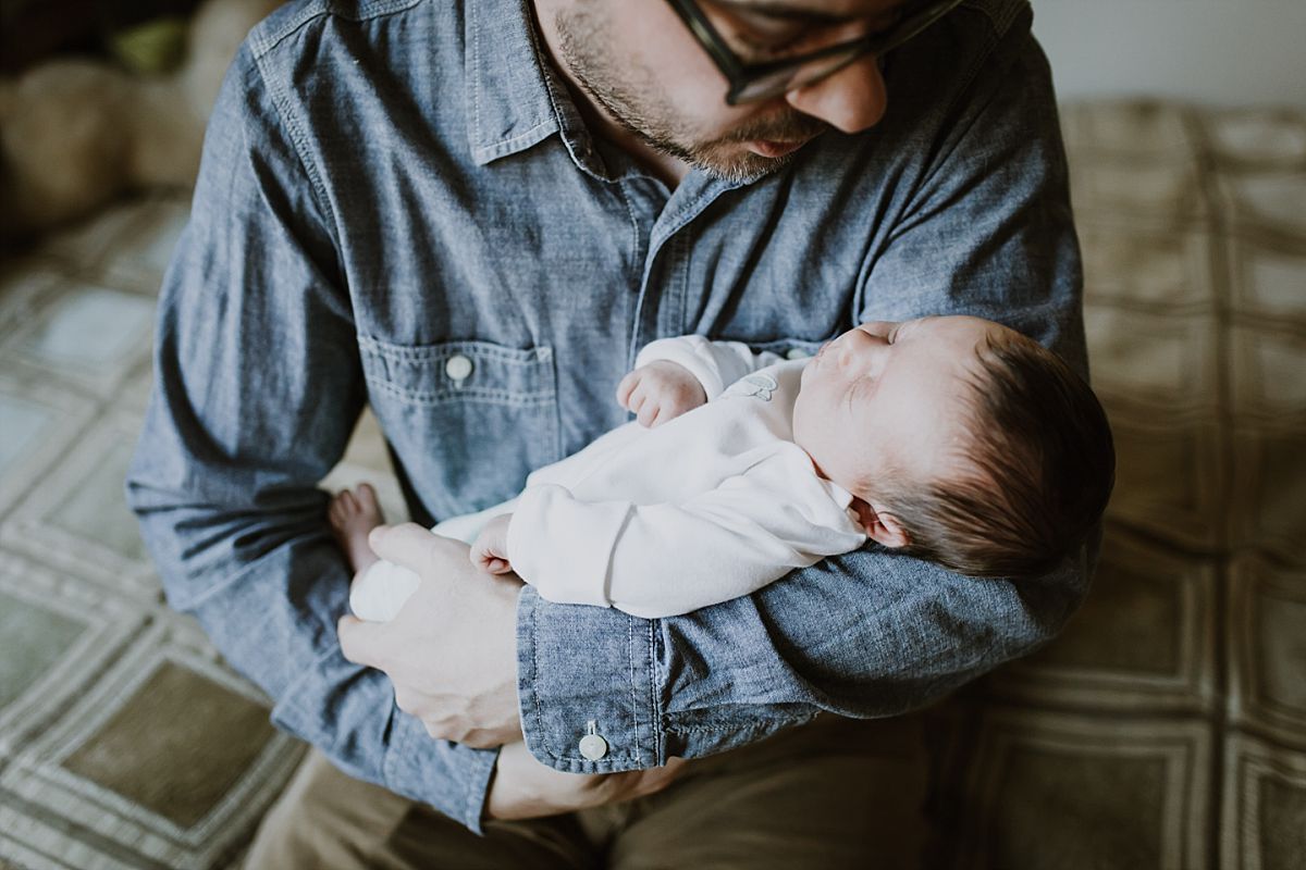 nyc family and newborn photographer dad holds newborn girl while sitting on bed