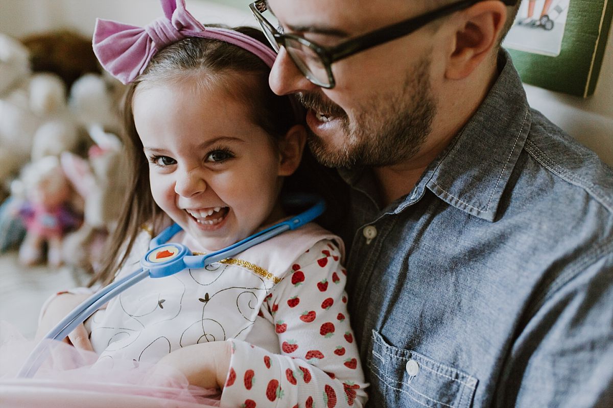 nyc family and newborn photographer dad and daughter sit on bed giggling for family photo session