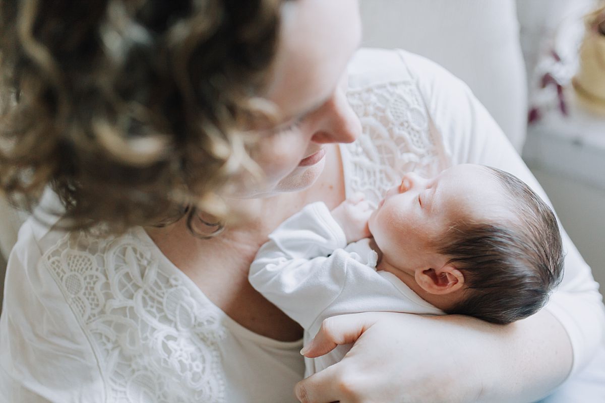 nyc family and newborn photographer mom holds newborn girl in rocking chair while newborn sleeps peacefully