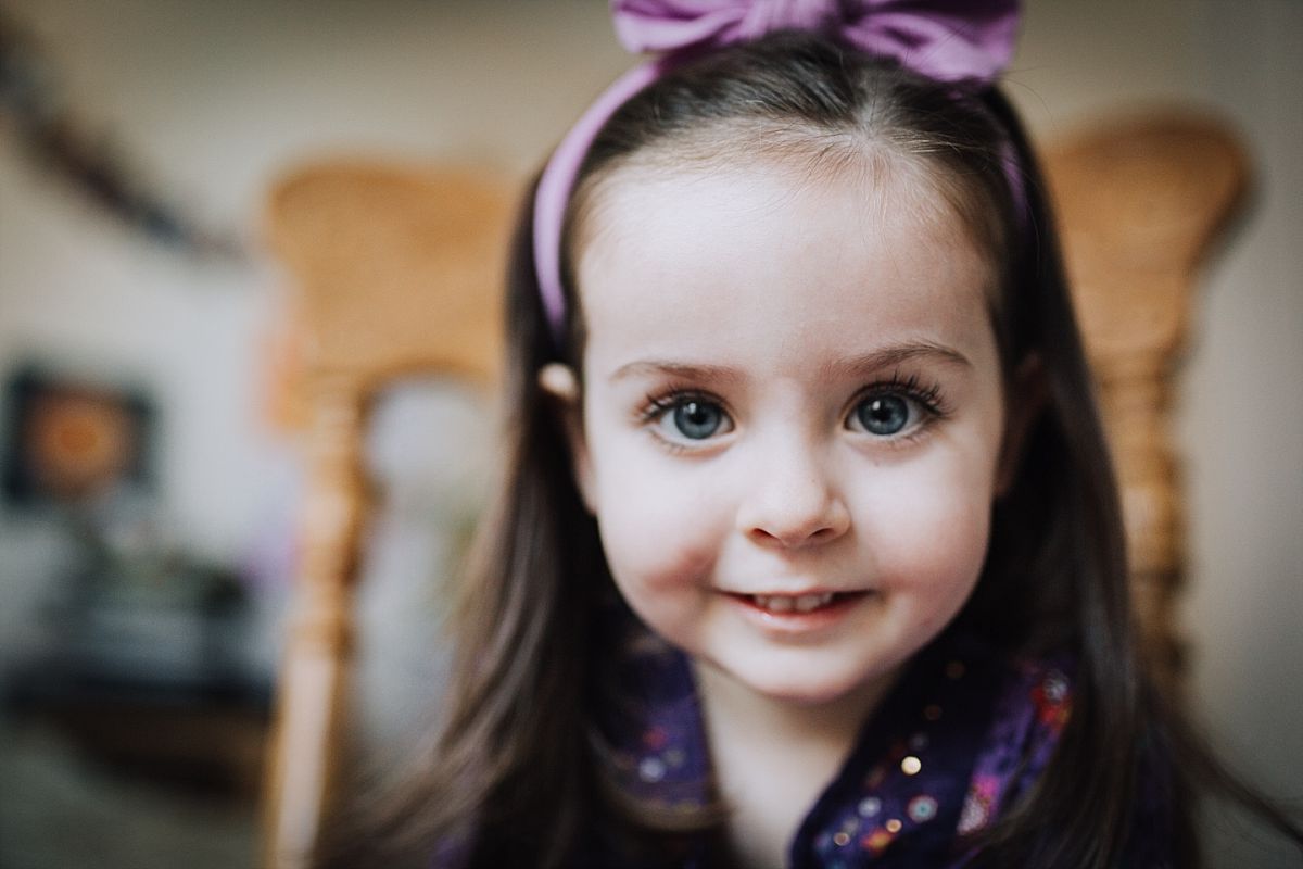 nyc family and newborn photographer daughter sits on wodden rocking chair and looks a camera for in home family session