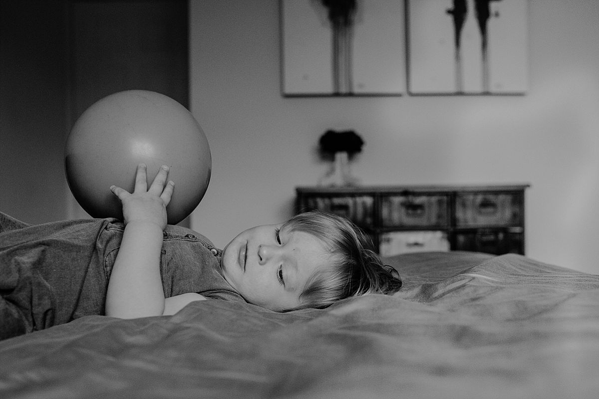 nyc family and newborn photographer son plays with big ball while laying on parents bed in fun nyc family session