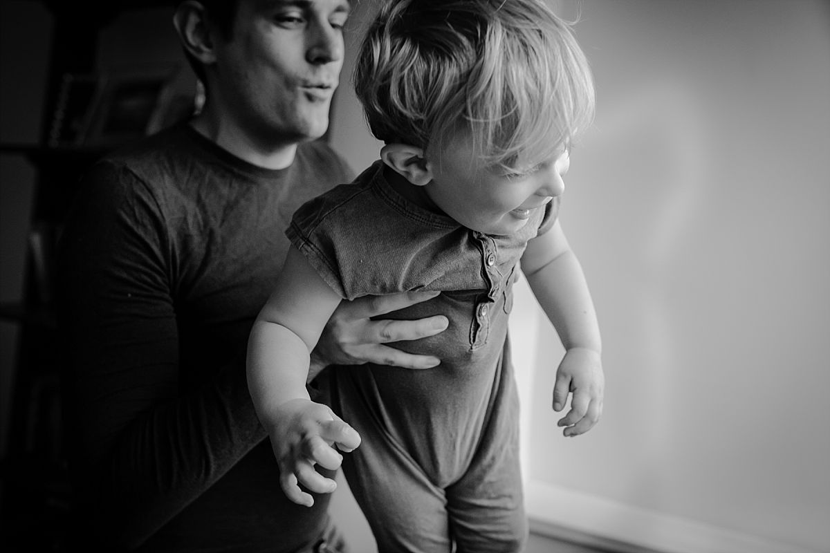 nyc family and newborn photographer dad playing with son in front of light window at home in nyc