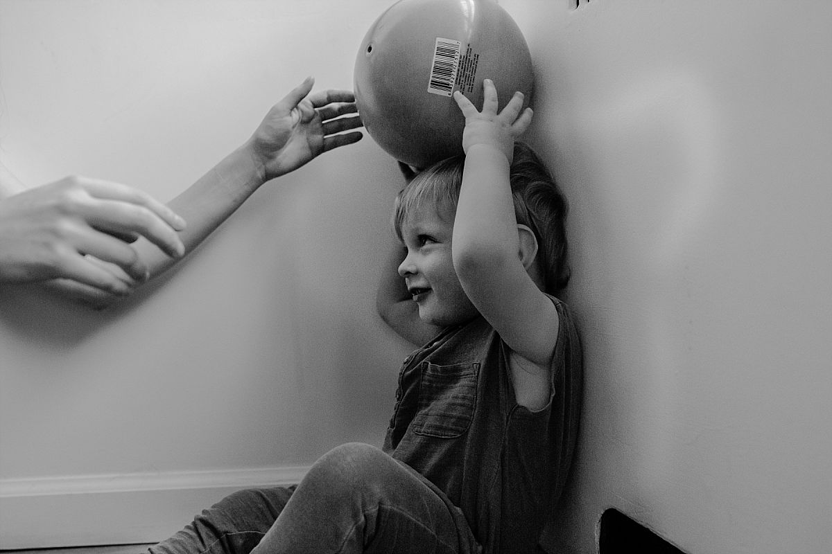 nyc family and newborn photographer toddler son leans against wall with ball over his head