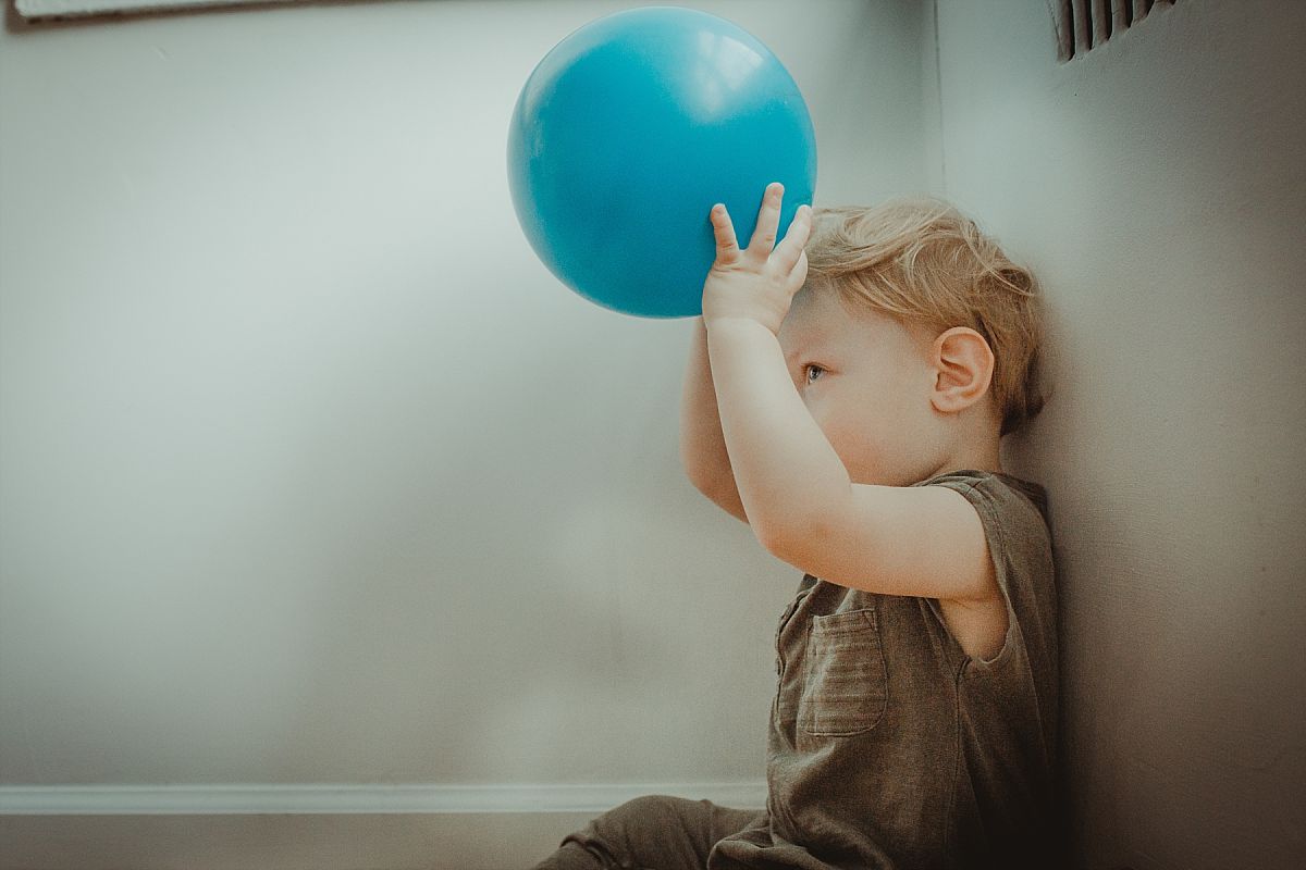 nyc family and newborn photographer son plays with blue blue ball against white wall