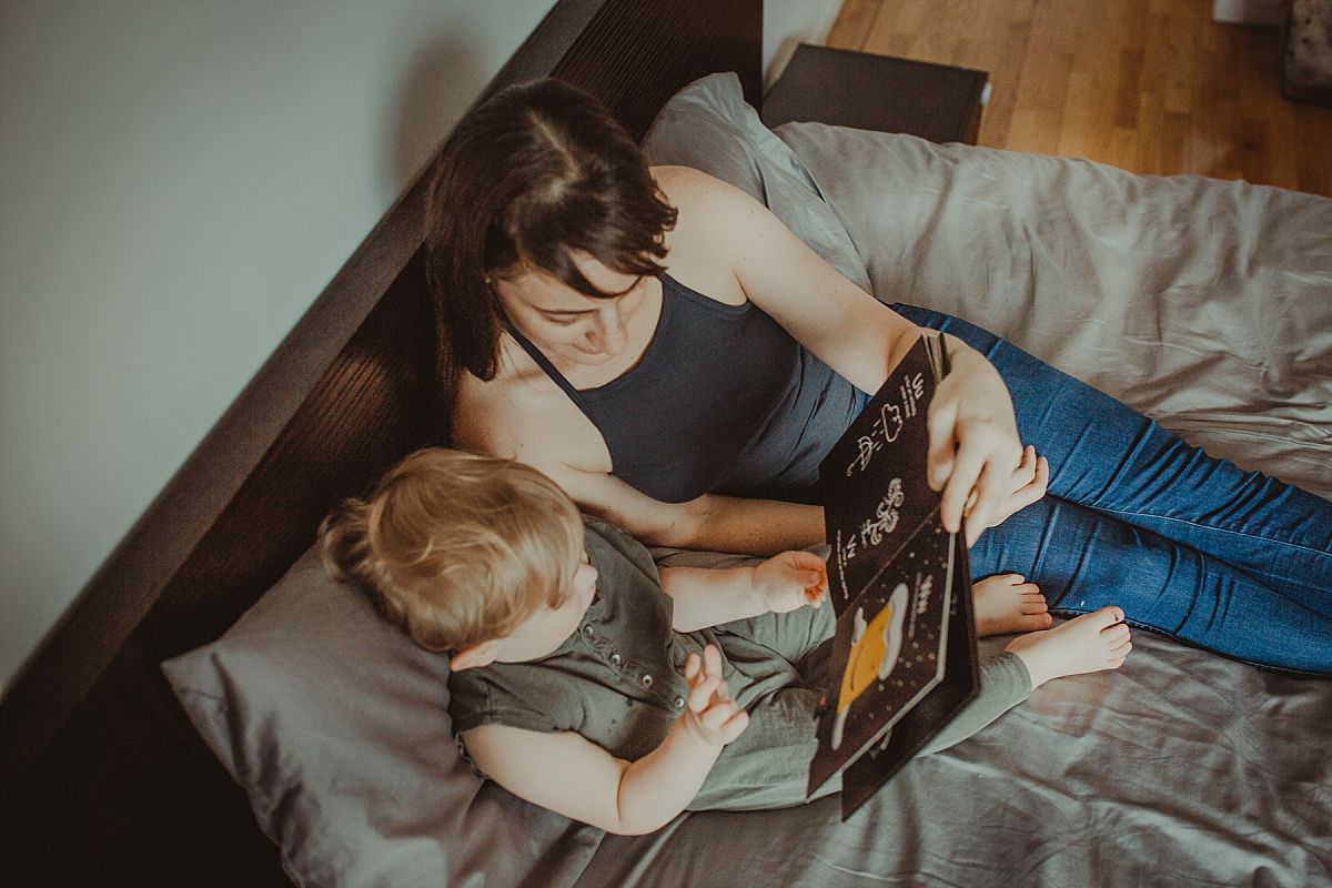 nyc family and newborn photographer mom and son enjoy reading book on bed at nyc in home session