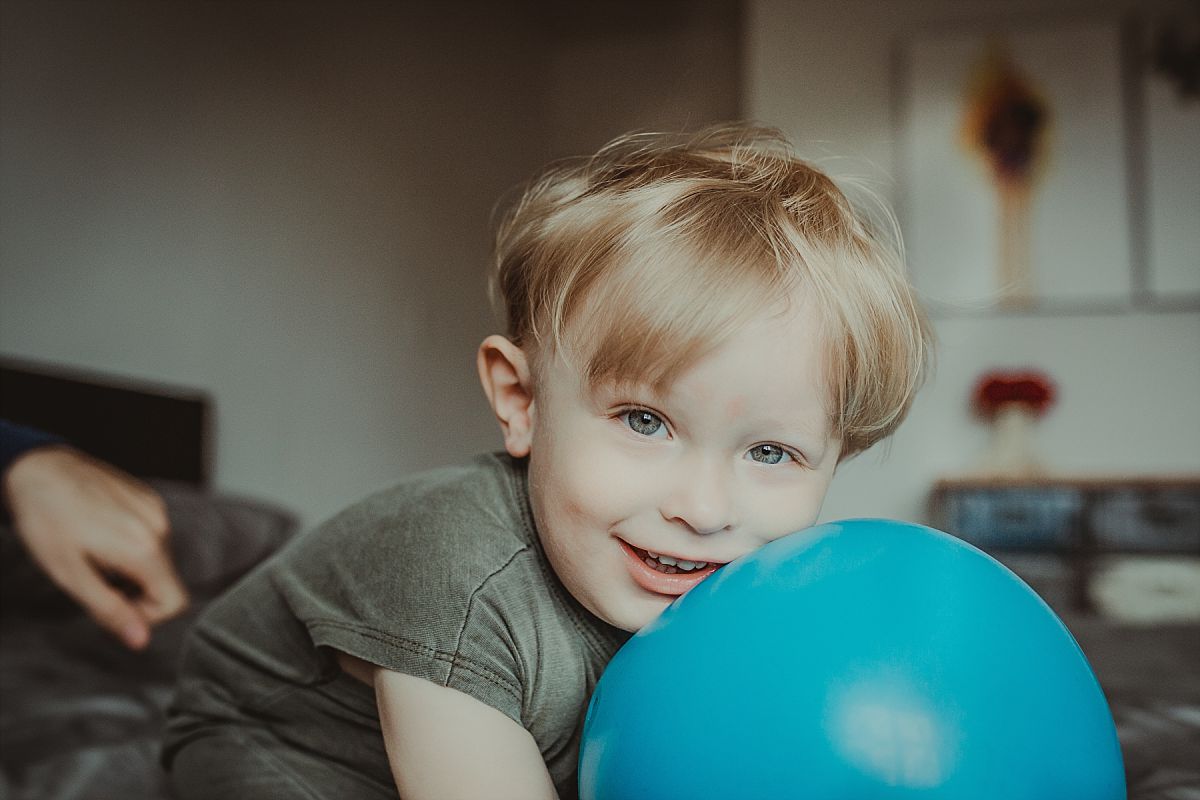 nyc family and newborn photographer boy leans on big blue ball with big smile