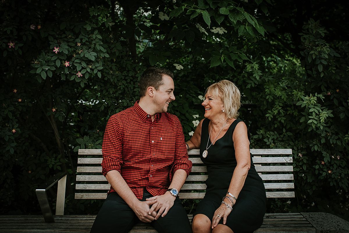 mom sits with son on park bench and son is in brightly colored red and block check shirt leaning at the high line in nyc. photo by Krystil McDowall photography