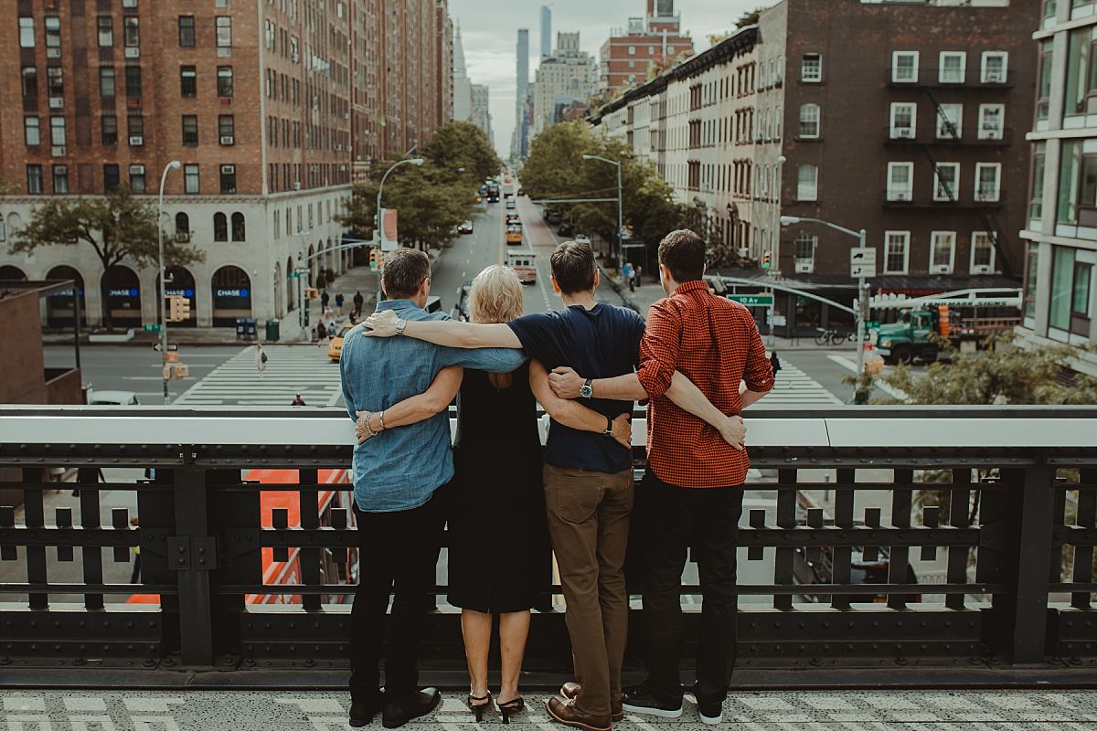 mom and three sons on bride at the highline overlooking busy nyc streets in nyc family photo session photo taken from behind with arms wrapped around each other
