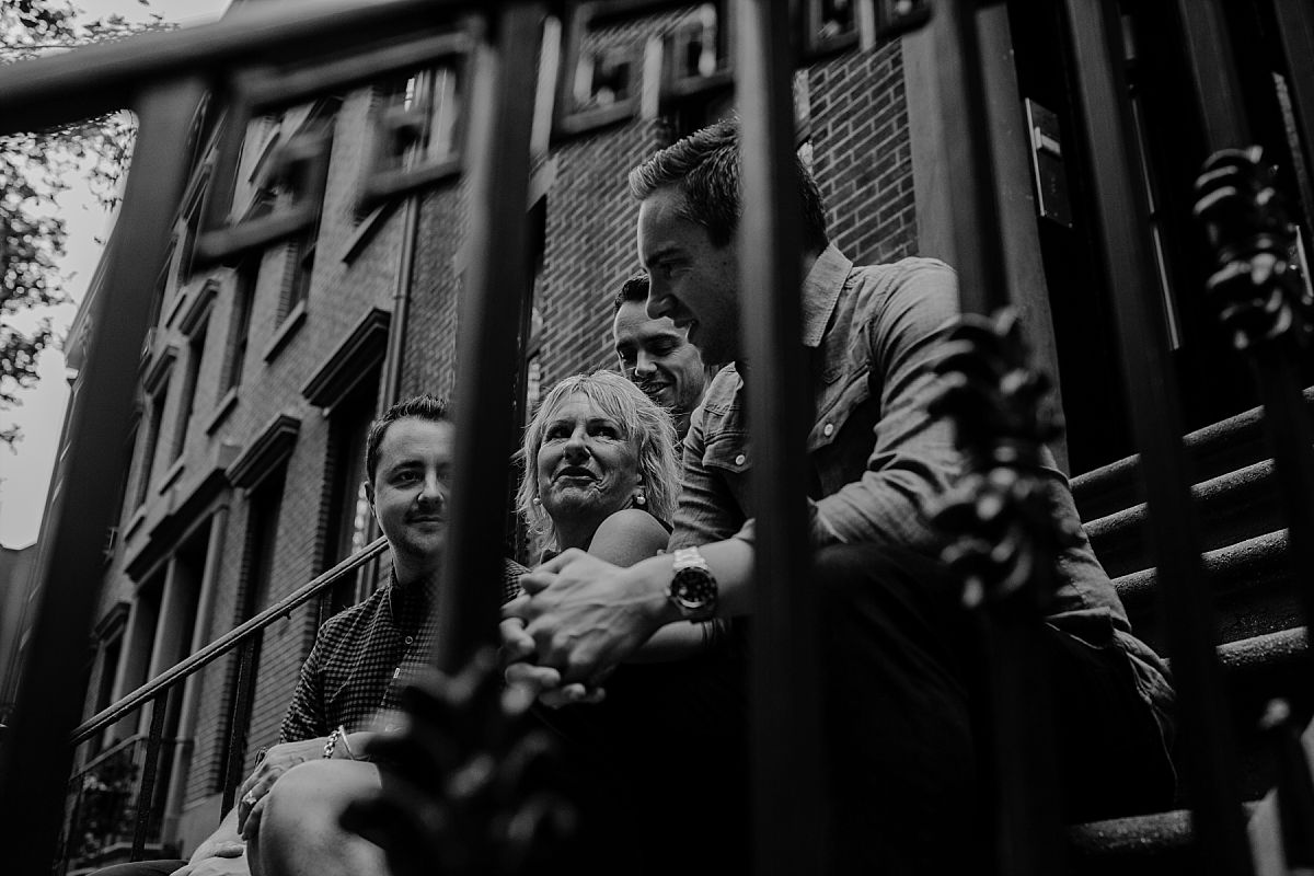 mom and three sons sitting on nyc stoop in chelsea and peaking through stoop rails in nyc family photo session