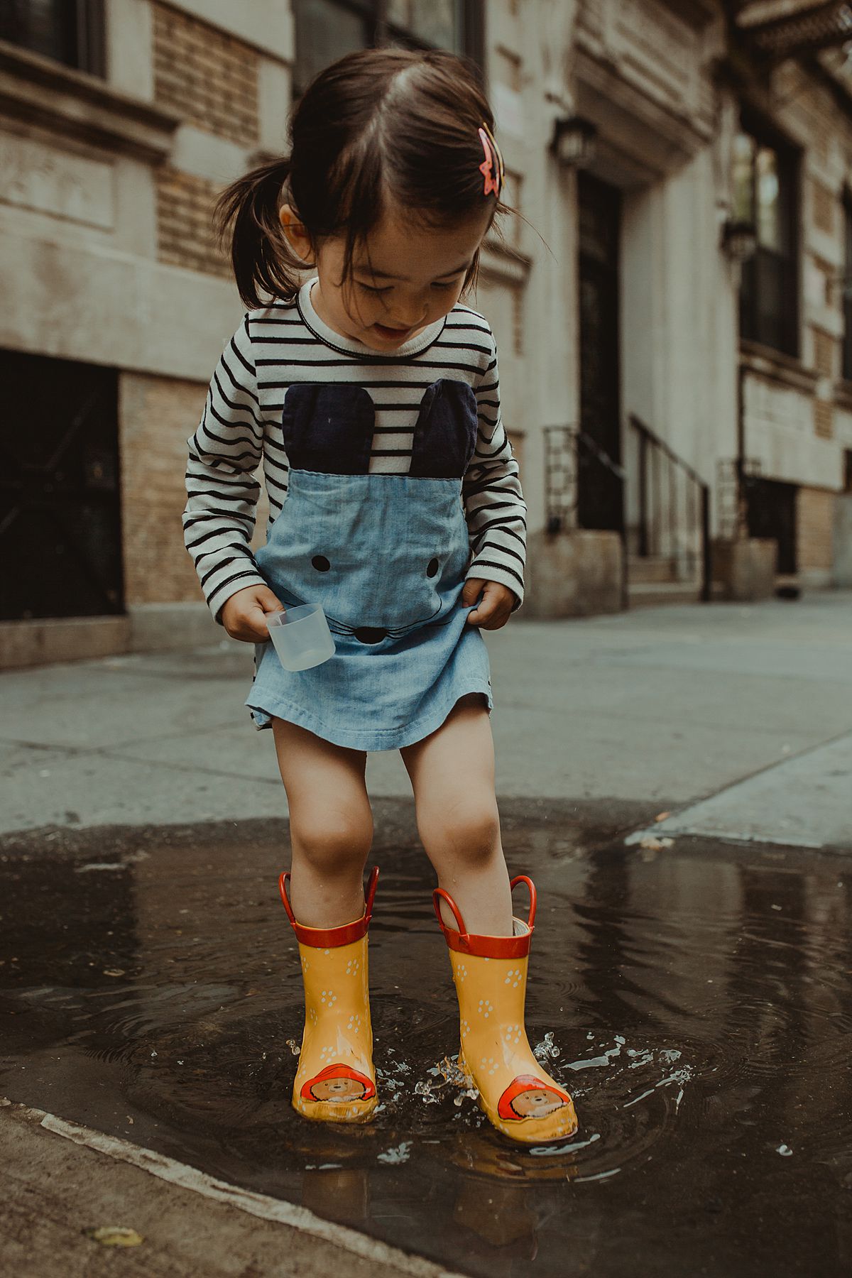 daughter splashing in puddle in yellow paddington bear rainboots. krystil mcdowall photography captures fun childhood moments