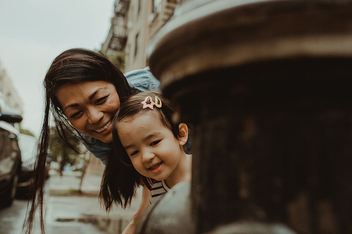 mom and daughter peek around fire hydrant on side of nyc street. capturing family moments and life nyc family and newborn photographer krystil mcdowall