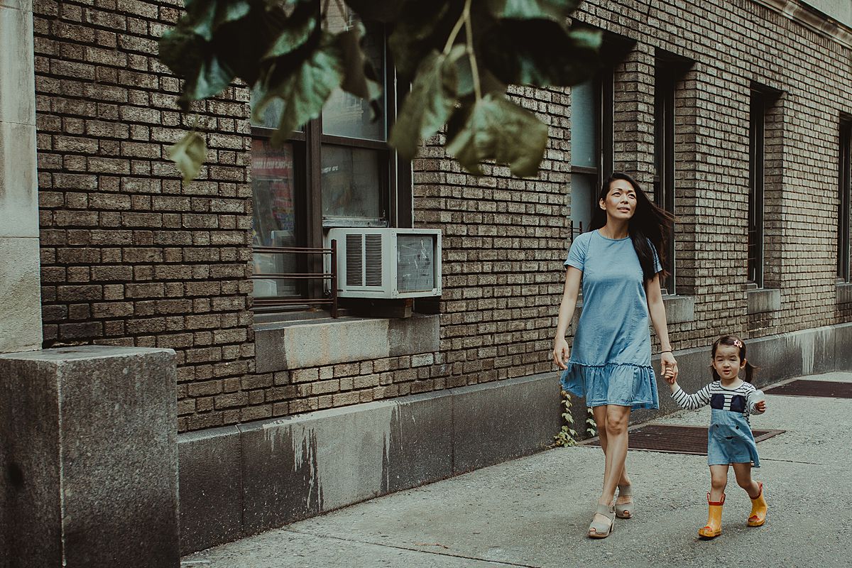 mom and daughter hold hands walking along nyc sidewalk in blue dresses. nyc family and newborn photographer krystil mcdowall capturing beautiful family moments to be treasured for a lifetime