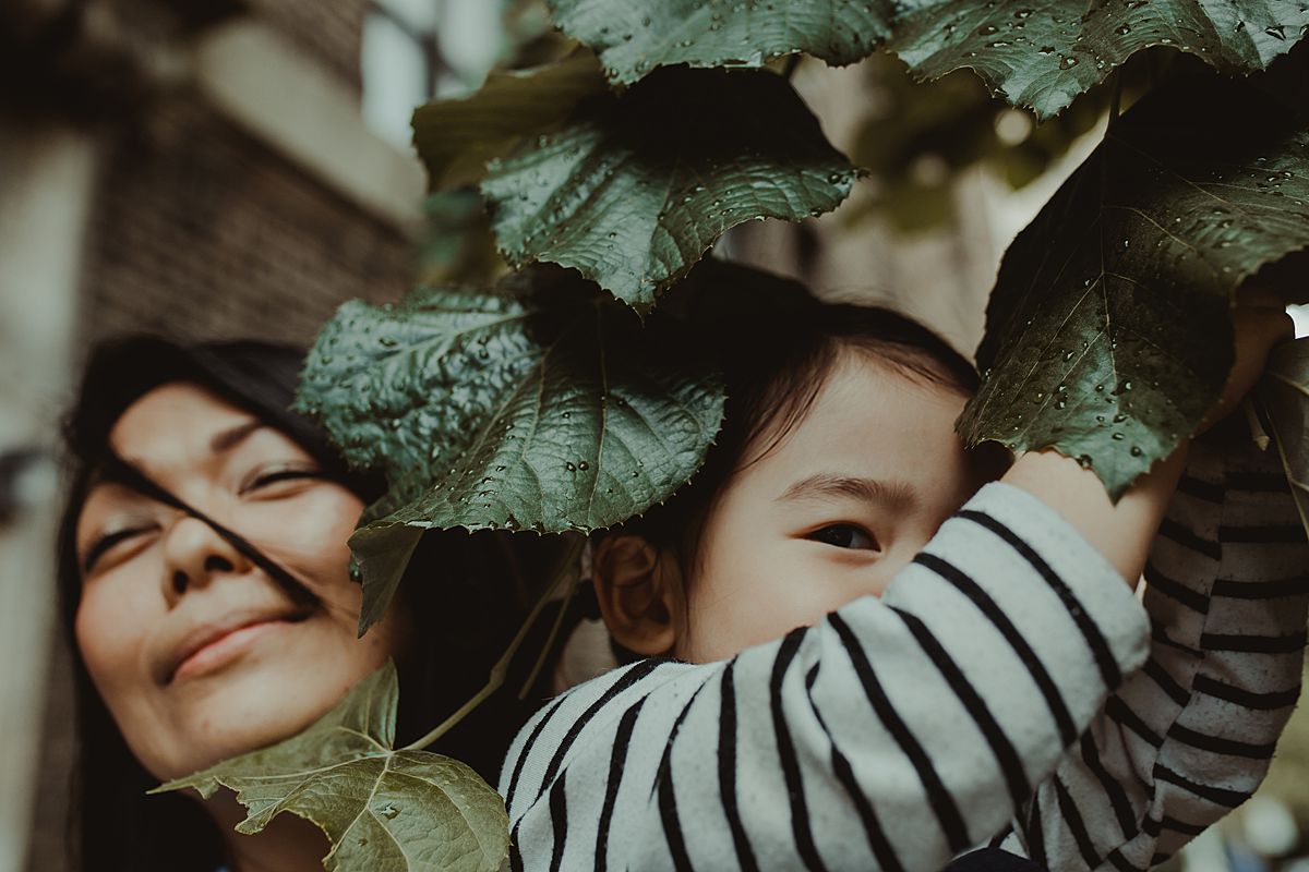 mom and daughter playing among tree leaves on nyc sidewalk. Krystil mcdowall photography capturing silly moments of your family