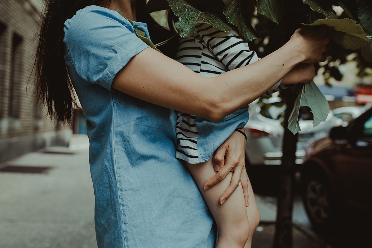 mom holding daughter so she can play with tree leaves. documentary lifestyle session by nyc family and newborn photographer krystil mcdowall