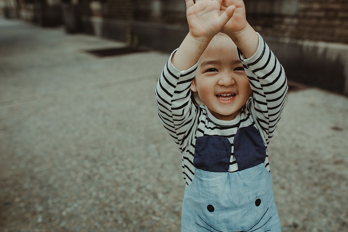 daughter holds hands over her head playing and shying away from the camera during documentary lifestyle session by nyc family and newborn photographer krystil mcdowall
