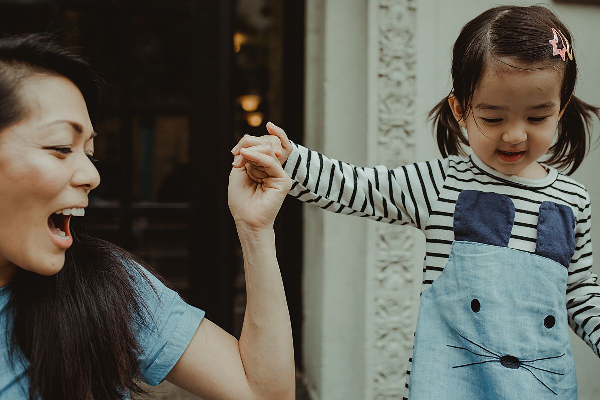 daughter and mom play together on balmy afternoon in front of nyc apartment block. capturing childhood moments