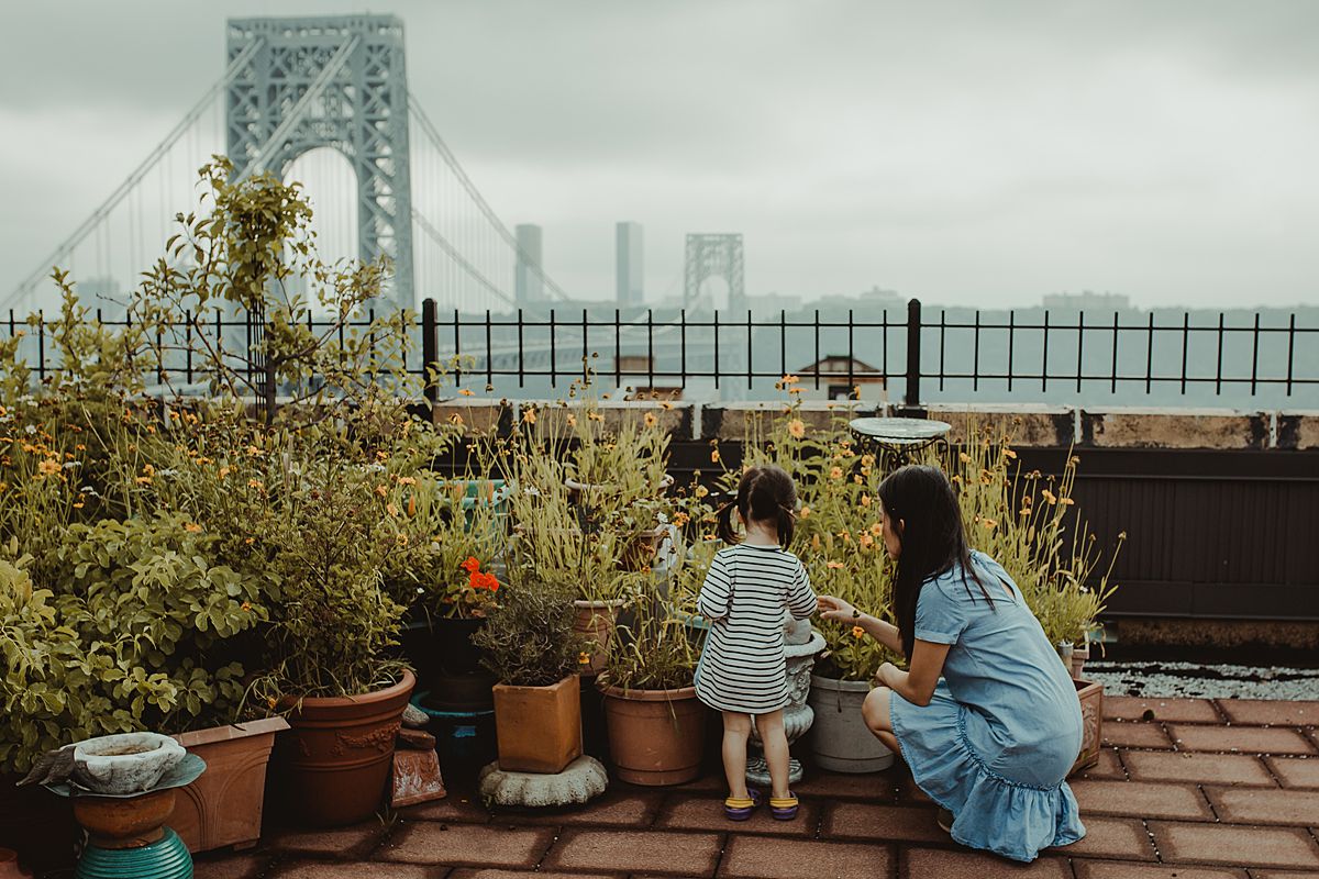 mom and daughter talk about the rooftop potplants while dressed in matching blue dresses on sunny nyc afternoon