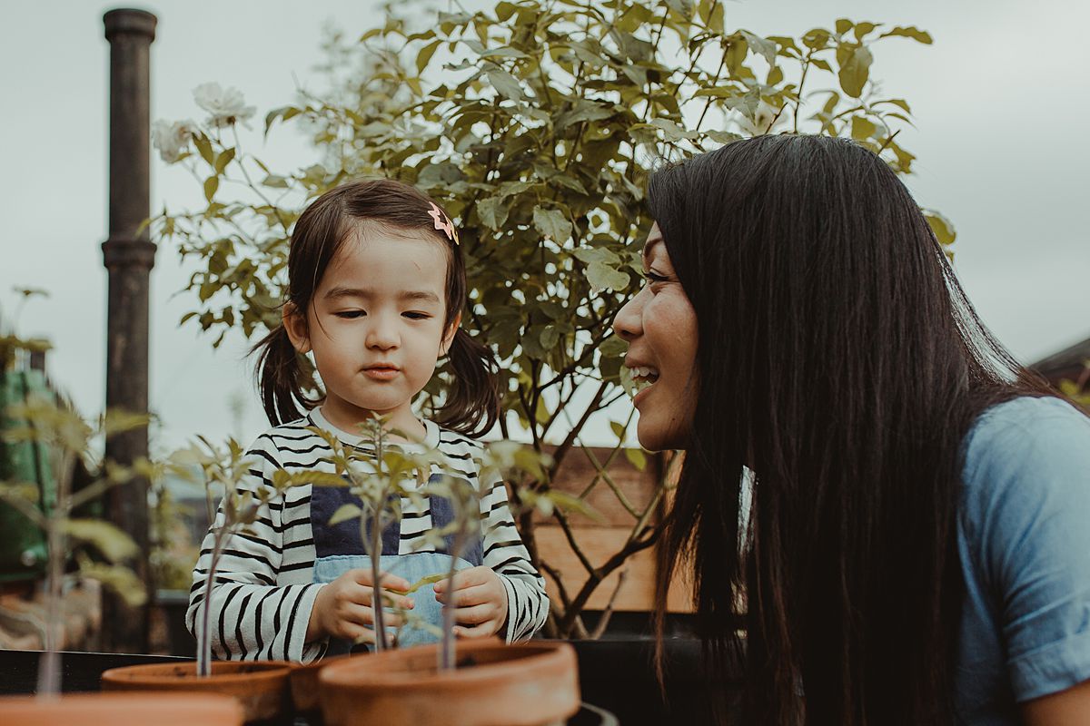 mom and daughter play with potplants and daughter is curious about plants and asks mom questions. capturing your fun family moments is nyc family and newborn photographer krystil mcdowall photography