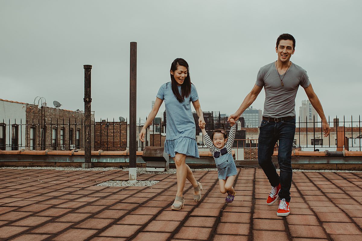mom, dad and daughter playing games on nyc rooftop with daughter swinging in the air