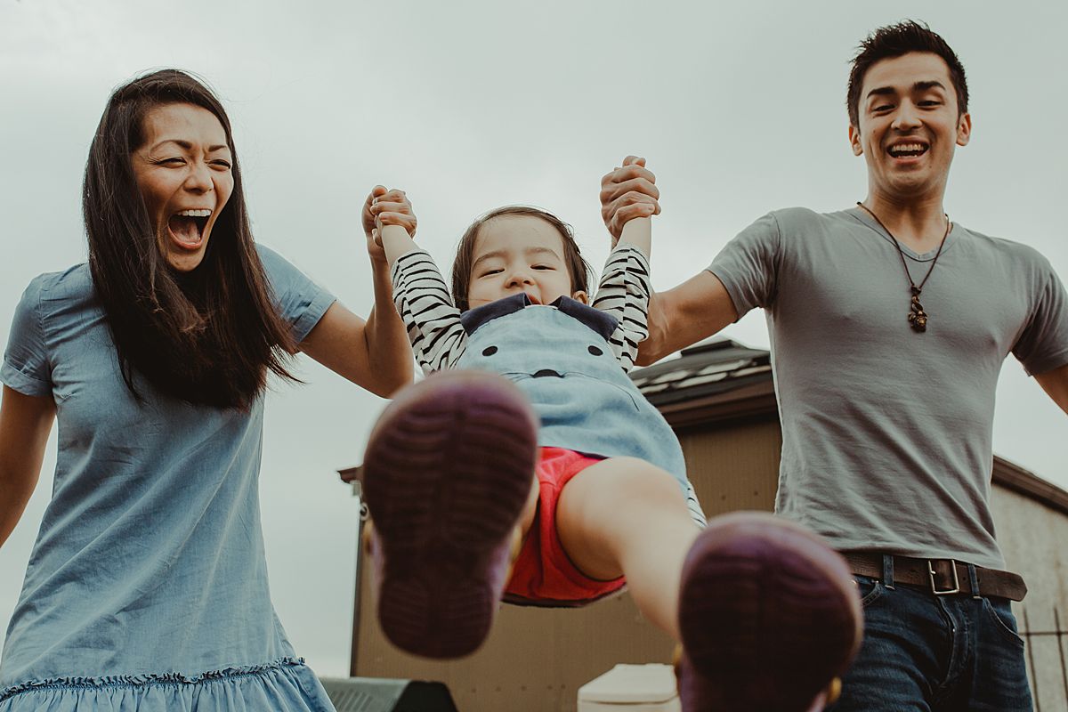 toddler laughing while mom and dad swing her in the air enjoying some fun family moments together in nyc