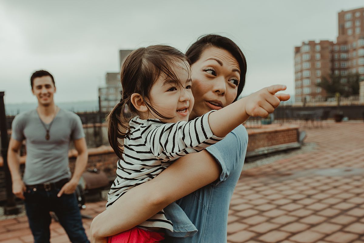 mom and daughter hold each other while daughter points to potplants and dad stands in the distance looking lovingly during documentary family session in nyc