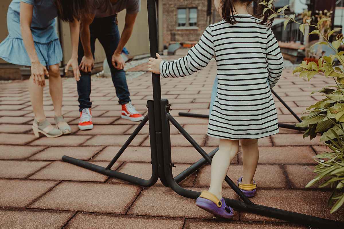 daughter swings around pole while mom and dad look on lovingly. photo taken during nyc family photoshoot