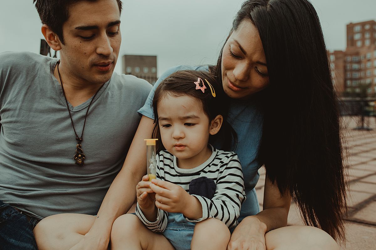 daughter plays with yellow hourglass while sitting on mom's lap during documentary nyc family photo shoot