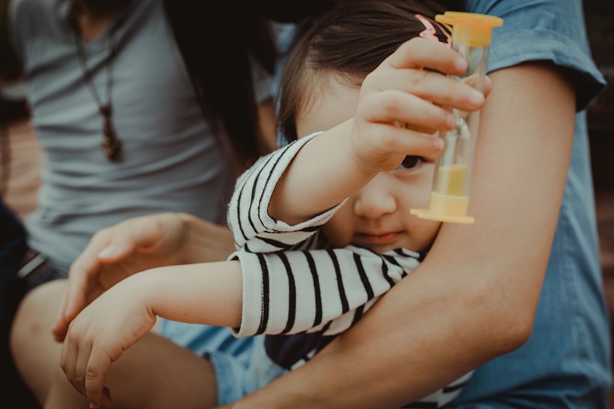 daughter sits and moms lap on nyc rooftop and daughter plays with yellow hourglass and dad sits next to them. Capturing real and genuine moments in nyc documentary family session by krystil mcdowall