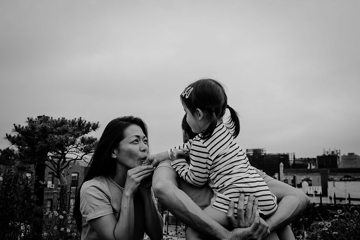 mom kisses daughter's hand while daughter enjoys piggy back from dad. image by krystil mcdowall photography in nyc family photoshoot