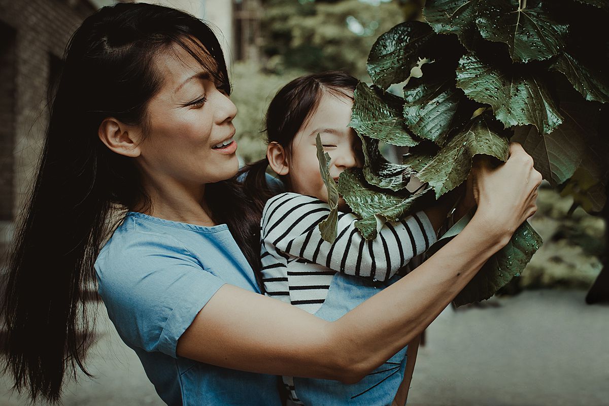 mom and daughter place with tree leaves on nyc sidewalk during documentary family session in nyc. Photo by Krystil McDowall Photography
