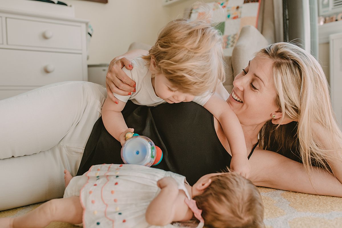 mom playing with toddler son and his toys and with newborn baby girl watching. nyc newborn session. Image by krystil mcdowall photography