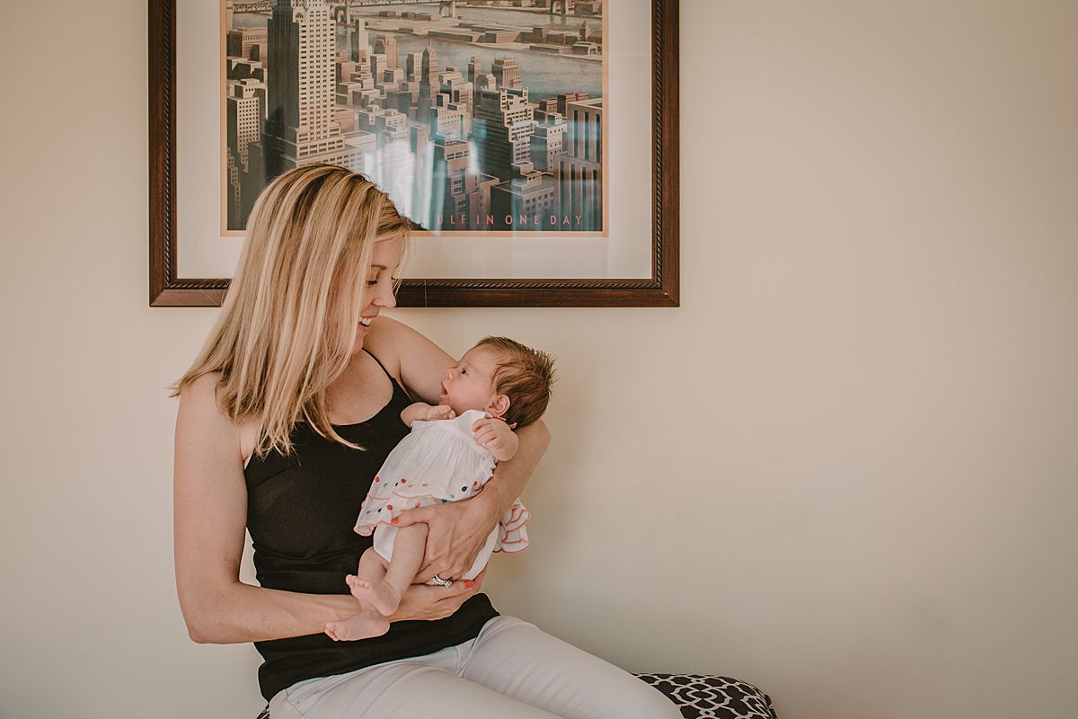 mom holding newborn baby girl sitting in front of nyc sign in family lifestyle session by nyc family and newborn photographer