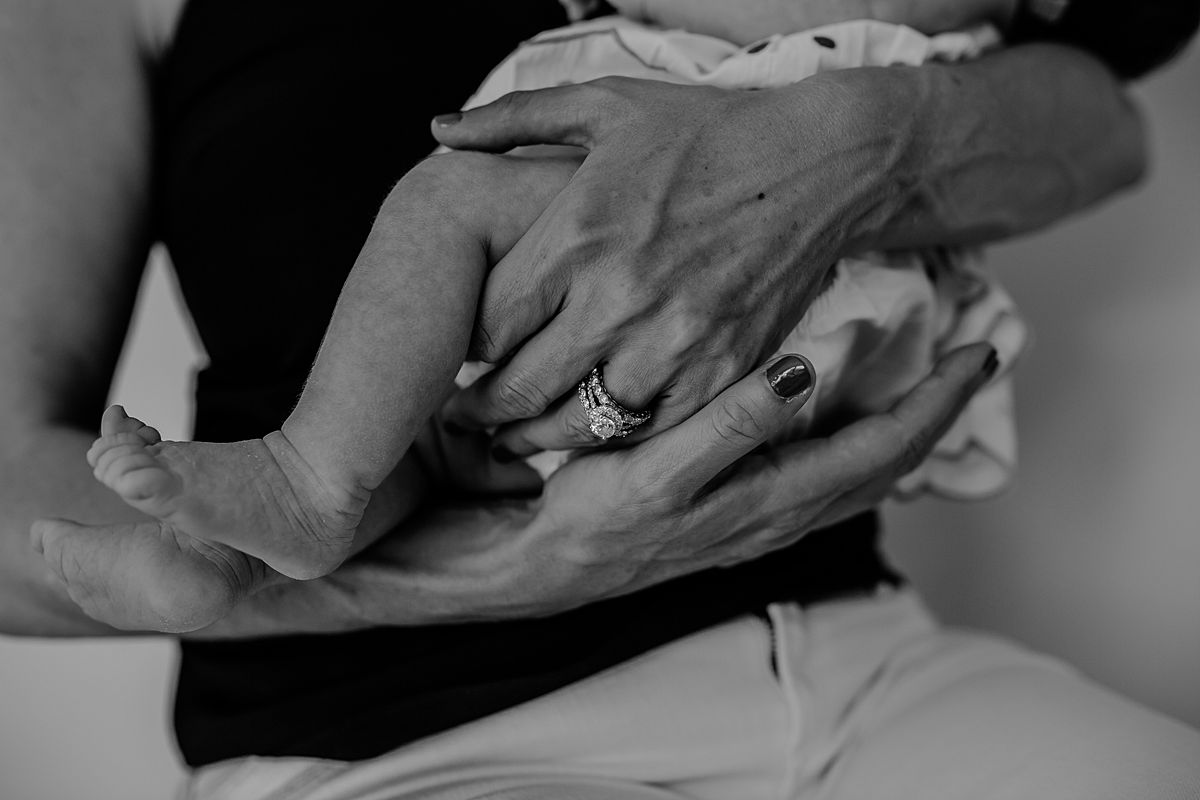 black and white image of newborn girl feet as they dangle while mom holds her. image by krystil mcdowall photography