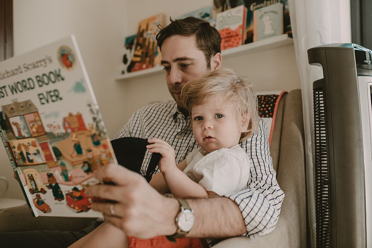 dad and son sitting in chair reading books together. Image by nyc family and newborn photographer krystil mcdowall photography