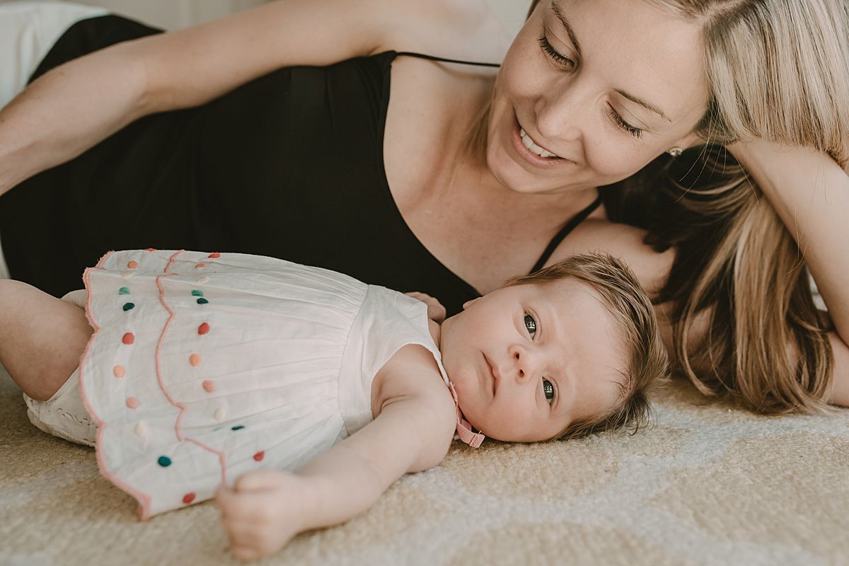 mom and baby girl lying on white and yellow rug capturing natural and real moments together in nyc newborn photography session in manhattan