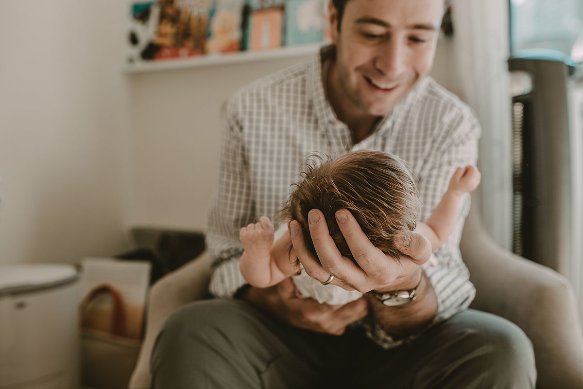 dad holding newborn baby girl sitting inrocking chair in family lifestyle session by nyc family and newborn photographer krystil mcdowall
