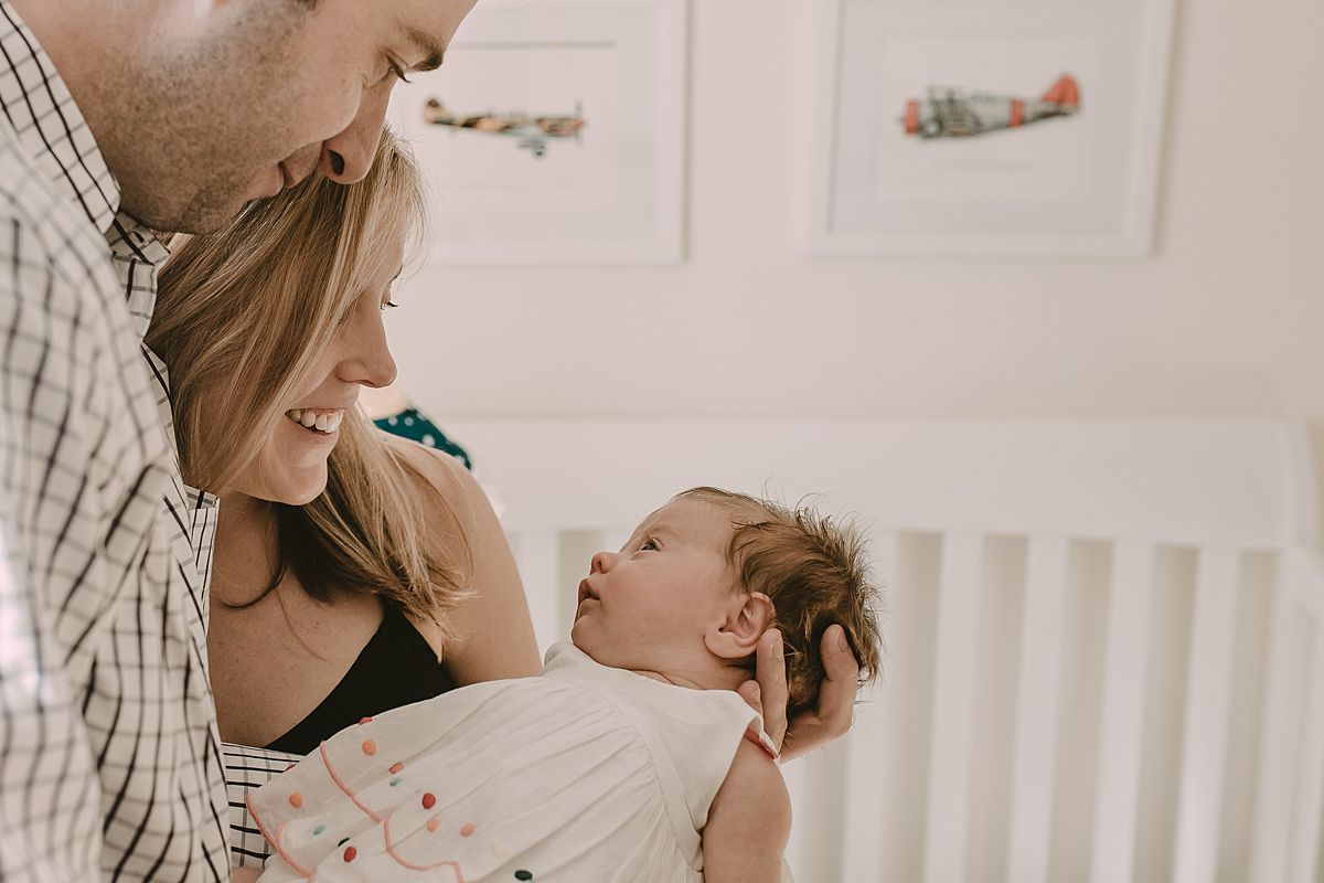 dad, mom look at beautiful daughter in newborn girl's room while standing in front of crib