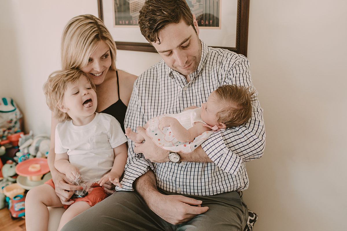 dad, mom, son and daughter enjoying cuddles in the kids room while son pokes his tongue out for photo. nyc family lifestyle session
