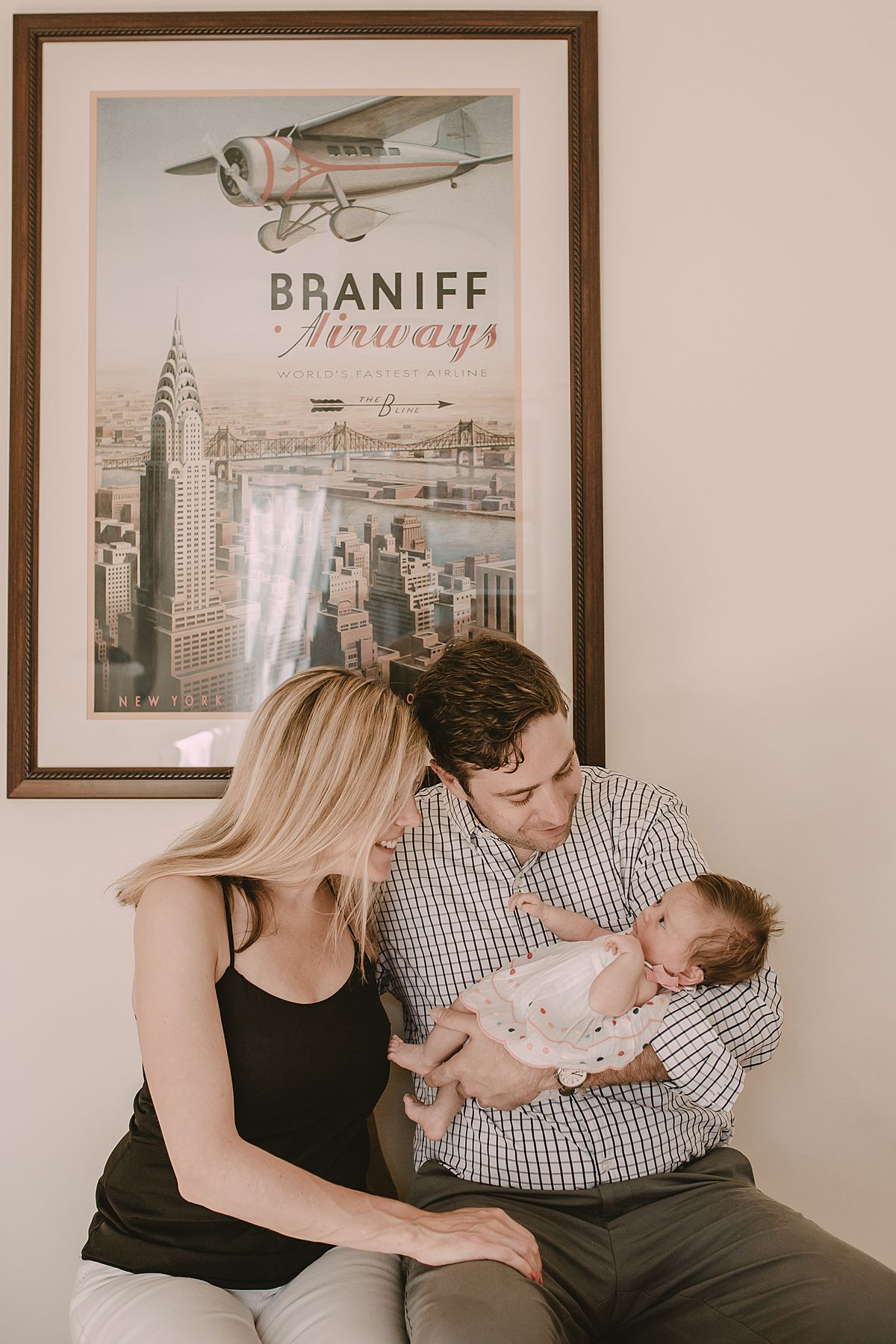mom and dad looking at newborn daughter with lots of love and smiles and in front of nyc wall hanging. Fun nyc newborn session by krystil mcdowall